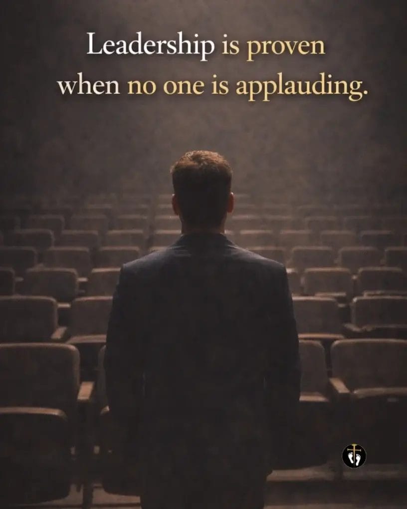 Man standing alone in a dimly lit auditorium symbolizing leadership and perseverance, with quote “Leadership is proven when no one is applauding”